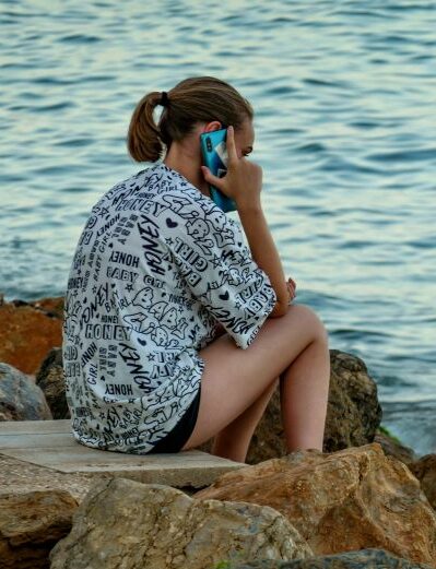 young woman engaged in DBT phone coaching by water